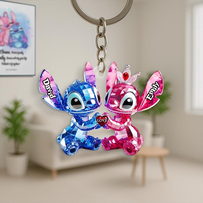 May include: A keychain with two faceted Stitch figures, one blue and one pink, holding a heart with the word "LOVE." The blue figure has the name "David" and the pink figure has the name "Emily" on their ears. A silver keyring is at the top.