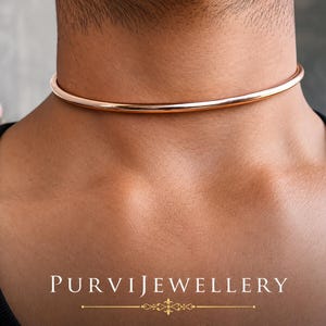 Könnte beinhalten: Ein roségoldenes Choker-Halsband. Die Halskette ist ein einfaches, glattes und abgerundetes Band, das eng am Hals anliegt. Das Bild enthält auch den Text "PURVIJEWELLERY" am unteren Rand.