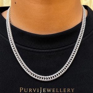 Puede incluir: Un collar de cadena plateada con un diseño tejido se muestra sobre un fondo negro. El collar se lleva alrededor del cuello. El texto "PURVIJEWELLERY" está en la parte inferior de la imagen.