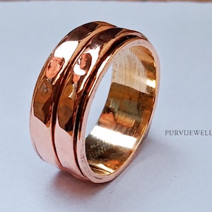 Op de afbeelding: Een ring van gepolijst koper met een brede band, een gehamerde textuur en een centrale horizontale groef die het oppervlak verdeelt. Het metaal heeft een warme, reflecterende roodbruine tint. De tekst PURVIJEWELLER is rechts zichtbaar.