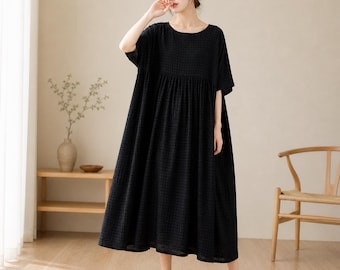 May include: A black, short-sleeved dress with a round neckline and a checkered pattern. The dress has a loose, flowing silhouette and falls to the mid-calf. The model is wearing beige shoes.