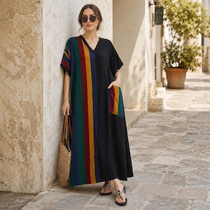 May include: A floor-length V-neck dress featuring a solid black side and a multi-colored vertical striped side in shades of green, blue, red, and yellow. The garment includes a single patch pocket on the black side with matching stripes.