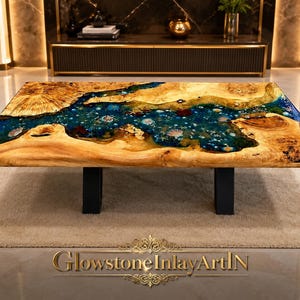Puede incluir: Una mesa de centro rectangular con un tablero de madera natural de borde vivo y un río central de resina azul translúcida. La sección de resina contiene conchas y estrellas de mar incrustadas. Patas de metal negro.