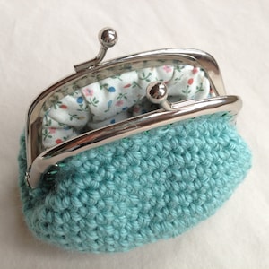 May include: A teal crocheted coin purse with a silver metal frame and a floral fabric lining.