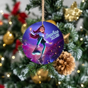 May include: A round, flat ornament featuring a digital illustration of a person with long dark hair, wearing a white shirt, dark shorts, and boots, floating against a purple background. The text "Sophia 2026" is printed in light blue script.