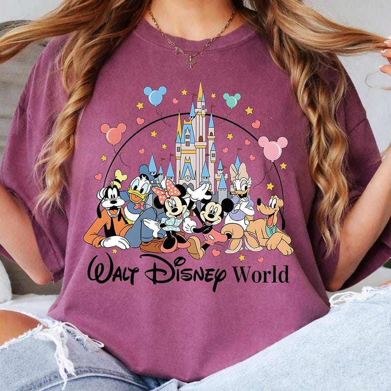 K&ouml;nnte beinhalten: Burgunderfarbenes T-Shirt mit einer Grafik von Disney-Figuren, darunter Micky und Minnie Maus, Donald Duck und Goofy, vor einem Schloss. Die Worte "Walt Disney World" sind unter den Figuren aufgedruckt.