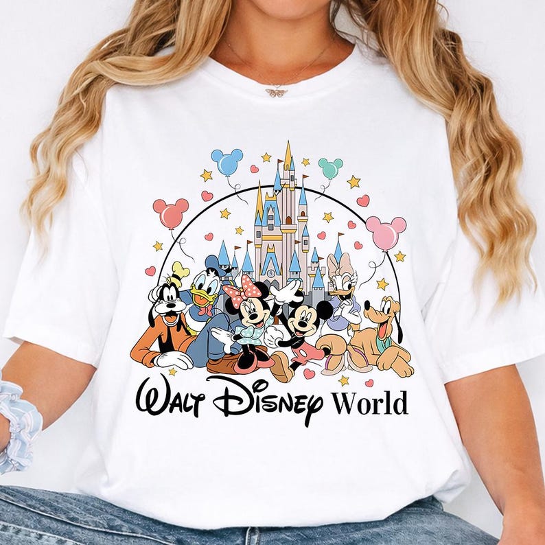 K&ouml;nnte beinhalten: Wei&szlig;es T-Shirt mit einer farbenfrohen Grafik von Disney-Figuren, darunter Mickey und Minnie Mouse, Donald Duck und Goofy, vor einem Schloss. Die Worte "Walt Disney World" sind unter den Figuren aufgedruckt.