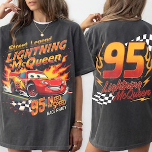 May include: Charcoal grey t-shirt with a Lightning McQueen design. The front features the red race car with flames and the text "Street Legend Lightning McQueen". The back displays the number 95 and the text "Lightning McQueen".