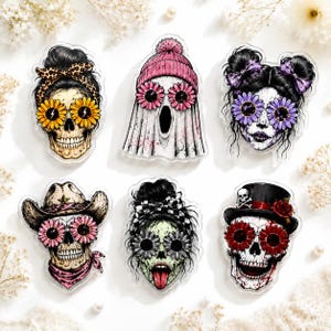 May include: A set of six decorative stickers featuring stylized skulls and a ghost. Designs include a skull with a leopard print headband, a ghost in a pink beanie, a skull with purple flower glasses, a cowgirl skull, a skull with a checkered bow, and a skull in a top hat.