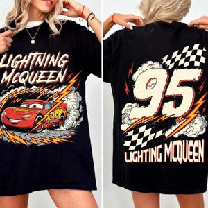 May include: Black t-shirt featuring Lightning McQueen from the Cars movie. The front graphic shows the red race car with the number 95, surrounded by lightning bolts and the text "Lightning McQueen." The back displays "95" and "Lightning McQueen" with a checkered flag.