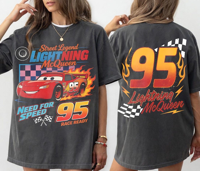 May include: Dark gray t-shirt featuring a graphic of Lightning McQueen from the movie Cars. The front design includes the text "Street Legend Lightning McQueen" and "Need for Speed 95 Race Ready". The back displays "95 Lightning McQueen".