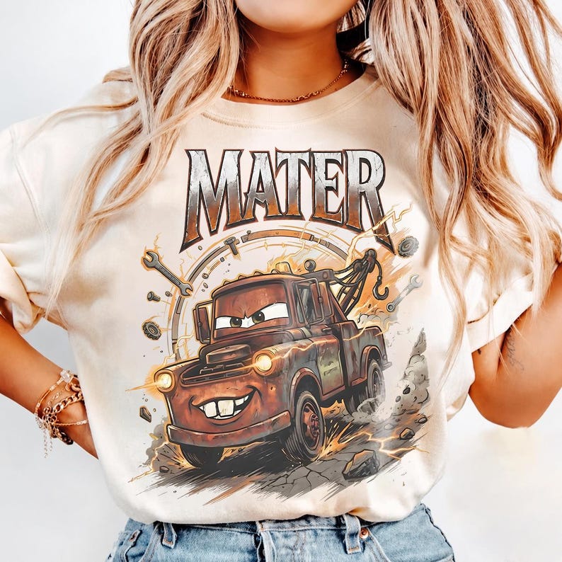 May include: Cream-colored t-shirt featuring a cartoon image of Mater from the movie Cars. The graphic shows Mater, a rusty tow truck, with the word "MATER" above. The design includes tools, lightning bolts, and a background resembling a clock.