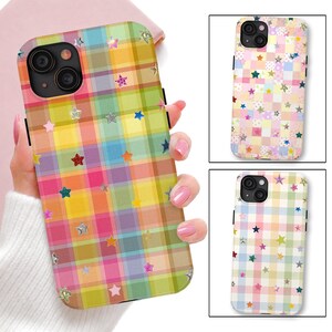 May include: A smartphone case featuring a vibrant, multi-colored plaid pattern in shades of yellow, pink, green, and blue. The surface is decorated with numerous small, scattered star shapes in various colors and metallic finishes.