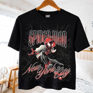 May include: Black t-shirt featuring a graphic of Spider-Man in a dynamic pose, with the words "SPIDER-MAN" and "New York City" in a stylized font. The design includes a red and white color scheme, with a spider web background.