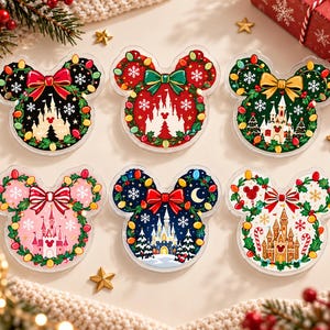 Peut inclure: Six décorations en acrylique en forme d'oreilles de souris, chacune présentant une illustration de château festif, des guirlandes lumineuses colorées, des nœuds et des flocons de neige. Les motifs incluent des fonds noir, rouge, vert, rose, bleu foncé et blanc.