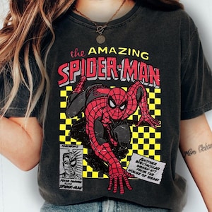 May include: Dark grey t-shirt with a vintage Spider-Man comic book graphic. The design features the text "the AMAZING SPIDER-MAN" in red and white, along with additional text and a yellow and black checkerboard pattern.