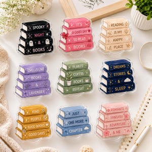 Pode incluir: Uma coleção de nove ornamentos de acrílico em forma de pilhas de livros, cada um composto por quatro livros de cores variadas com textos impressos como Spooky Night & Books, It's A Good Day To Read Books e Reading Is My Happy Place.