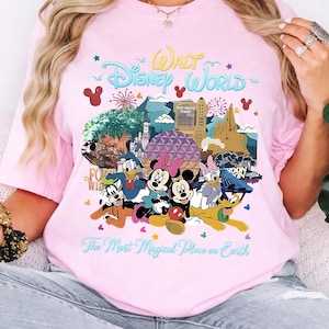 K&ouml;nnte beinhalten: Hellrosa T-Shirt mit einem farbenfrohen Aufdruck von Disney-Figuren und Wahrzeichen, darunter Micky und Minnie Maus, Donald Duck und das Hollywood Tower Hotel. Der Text lautet "Walt Disney World" und "The Most Magical Place on Earth."