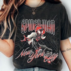 May include: Dark gray t-shirt featuring a Spider-Man graphic. The design includes the words "SPIDER-MAN" in red and white, and "New York City" in a stylized script. The illustration depicts Spider-Man in a dynamic pose.
