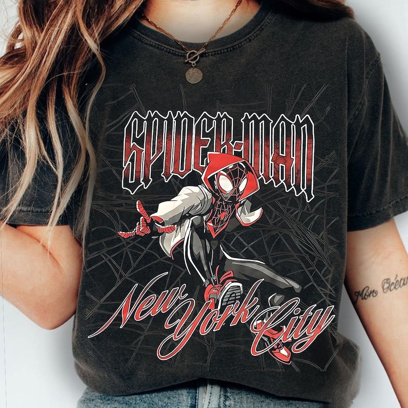 May include: Dark gray t-shirt featuring a Spider-Man graphic. The design includes the words "SPIDER-MAN" in red and white, and "New York City" in a stylized script. The illustration depicts Spider-Man in a dynamic pose.