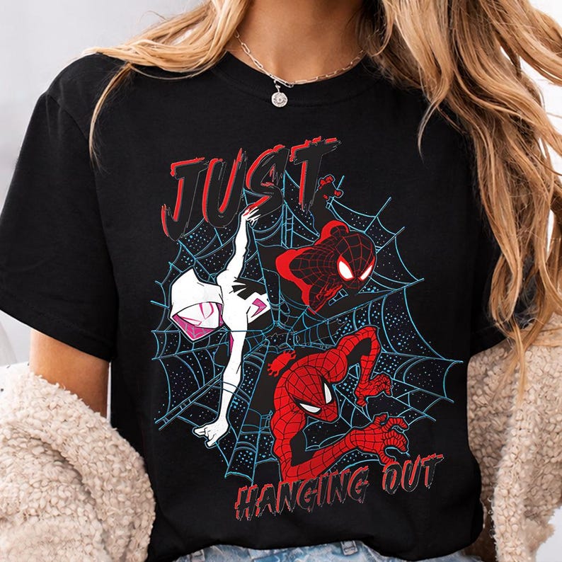 Puede incluir: Camiseta negra con un gr&aacute;fico de personajes de Spider-Man en rojo, negro y blanco, con las palabras "JUST HANGING OUT" en rojo. El dise&ntilde;o incluye un fondo de telara&ntilde;a azul.