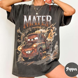 May include: Dark gray Mater graphic t-shirt. The design features the word "MATER" above a cartoon image of Mater the tow truck, with lightning bolts and tools in the background. The shirt has a vintage, worn look.