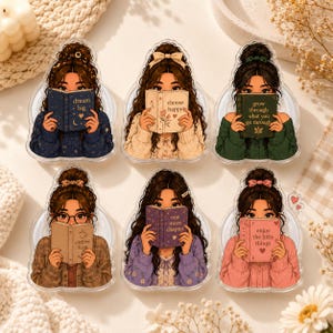 May include: Six acrylic charms featuring illustrations of individuals with long brown hair in various hairstyles, each holding a book. The books display the text: dream big, choose happy, grow through what you go through, coffee first, one more chapter, and enjoy the little things.
