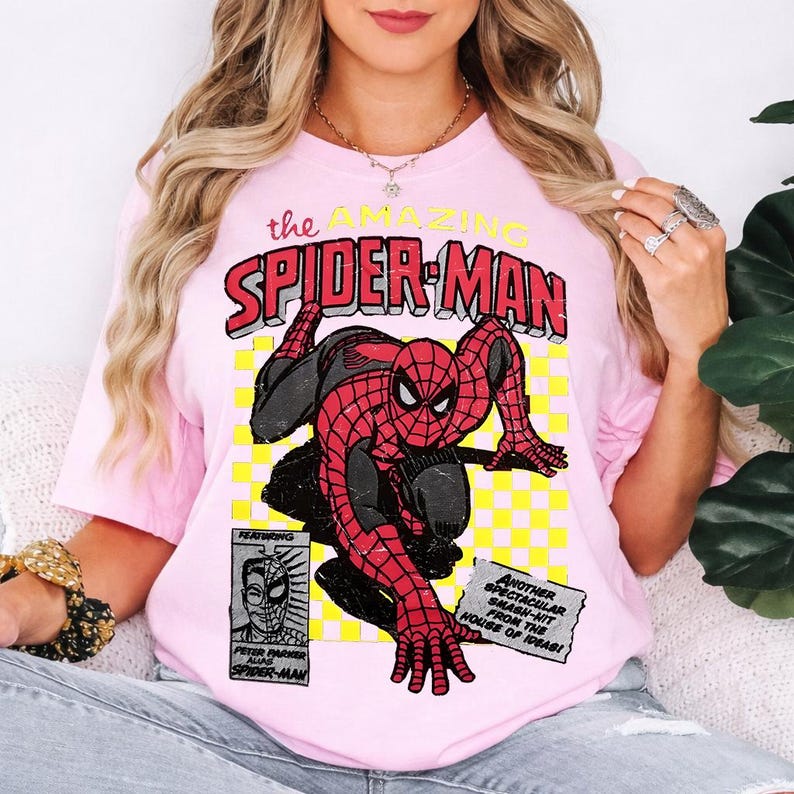 May include: Pale pink t-shirt with a Spider-Man comic book graphic. The design features the words "the AMAZING SPIDER-MAN" in red and yellow, plus additional text and a small illustration of Peter Parker.