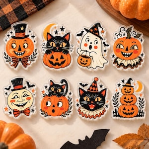 May include: A set of eight acrylic Halloween-themed charms featuring illustrations of orange pumpkins, black cats, a white ghost, and a moon. The designs include various festive elements like top hats, bows, stars, bats, and collars in orange and black.