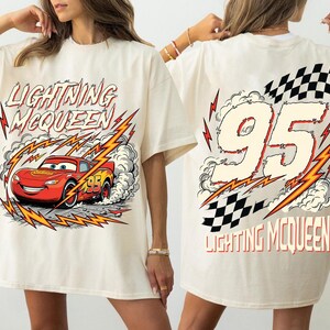 May include: Cream-colored t-shirt featuring Lightning McQueen from the Cars movie. The front graphic shows the red race car with the text "LIGHTNING McQUEEN". The back displays the number "95" with a checkered flag and the text "LIGHTNING McQUEEN".
