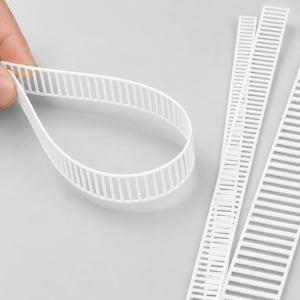 May include: White plastic ladder-style cable ties featuring a flexible, bendable design. The strips have a series of evenly spaced rectangular openings along their length. The text Good Flexibility Bendable is printed at the top of the image.