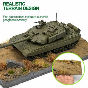 May include: An olive green model tank with a long barrel and detailed features, set on a diorama base with realistic terrain. The base includes brown dirt, patches of grass, and small rocks. The text "REALISTIC TERRAIN DESIGN" is visible.