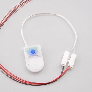 May include: A white plastic battery holder with a blue push button, connected to a thin white wire loop and two white plastic connectors. Several long, thin red and black wires extend from the connectors, ending in small exposed metal tips.