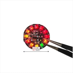Puede incluir: Una placa de circuito impreso circular negra con m&uacute;ltiples LED rojos, naranjas y verdes iluminados dispuestos en anillo. El componente mide 1,8 cm de di&aacute;metro, seg&uacute;n lo indicado por el texto y el gr&aacute;fico de doble flecha.