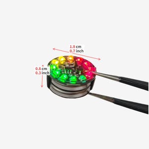 Puede incluir: Un m&oacute;dulo LED circular con luces rojas, amarillas y verdes, sostenido por pinzas. El dispositivo mide 1,8 cm de di&aacute;metro y 0,8 cm de altura, seg&uacute;n lo indicado por el texto de medici&oacute;n y las flechas visibles en el componente.