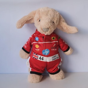 May include: A plush beige rabbit toy wearing a red racing suit with white accents. The suit features logos including HP, Shell, and Ceva, along with the number 44, a British flag, and the text Lewis Hamilton printed on the front chest area.