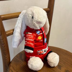 Side view of a bunny plush wearing a red one-piece racing jumpsuit, showing the sleeve fit, leg openings and sporty collector styling; clothes only, plush not included.