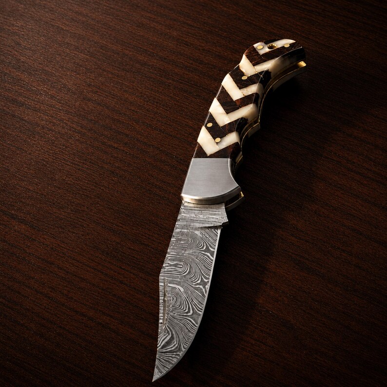 Folding pocket knife with polished steel blade and colorful inlay handle displayed on dark wood.