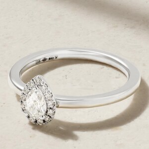 Op de afbeelding: Een zilveren ring met een peervormige centrale steen omringd door een halo van kleine ronde steentjes. De ringband is glad en gepolijst, met een duidelijk keurmerk zichtbaar aan de binnenzijde van de metalen schacht nabij de zetting.
