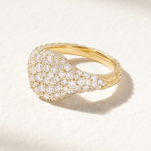 May include: A gold ring featuring a rounded, diamond-covered top. The ring's band has a textured pattern. The small diamonds are closely set, creating a sparkling effect. The ring is displayed on a white background.