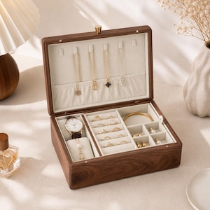 May include: Open wooden jewelry box with multiple compartments. The box contains a watch, rings, necklaces, earrings, and a bracelet. The box is made of dark wood and has a light-colored interior.