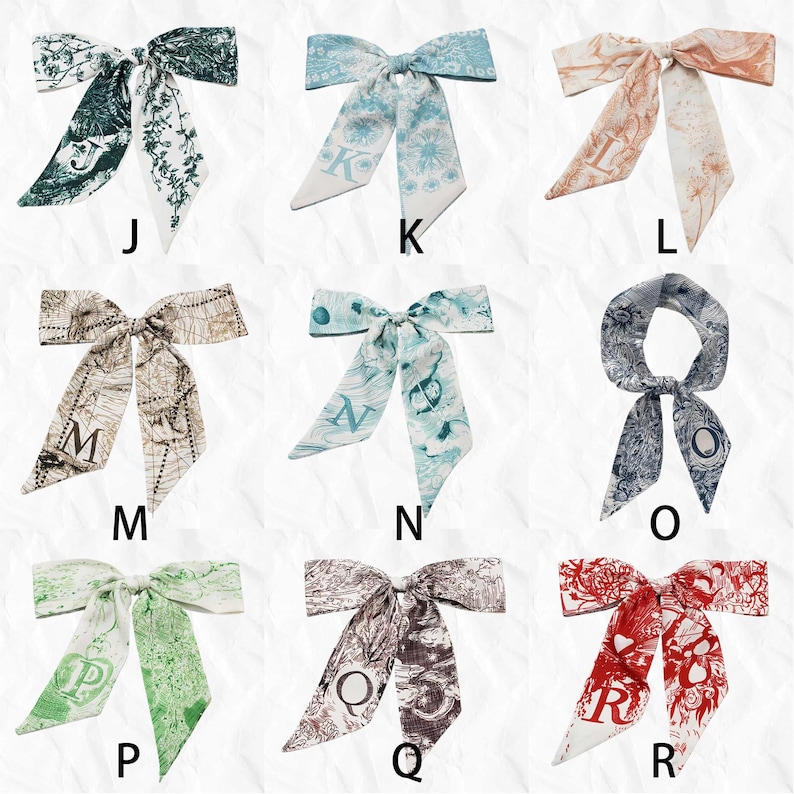 May include: Collection of silk scarves with various designs and initial letters. The scarves feature floral, map, and abstract patterns in colors like green, blue, brown, and red. Each scarf has a bow shape with long, flowing ends.