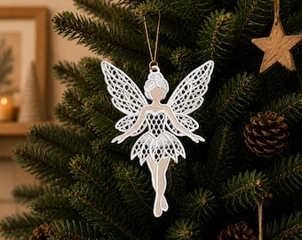 May include: A white and tan fairy Christmas ornament with intricate lace-like detailing. The fairy has outstretched wings and is hanging from a gold string on a Christmas tree. The ornament is surrounded by pine needles and other Christmas decorations.