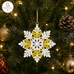 Può includere: Un ornamento sospeso a forma di fiocco di neve con un intricato ricamo in filo giallo brillante e bianco. Il design include motivi floreali simmetrici e dettagli in filigrana, sospeso tramite un sottile cordino dorato a un ramo di pino.