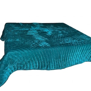 May include: A rectangular teal velvet quilt featuring a repeating fan-shaped stitched pattern across the surface. The fabric has a soft, reflective sheen characteristic of velvet, with deep blue-green tones and a finished edge border.