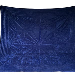 May include: A deep navy blue velvet quilt featuring a geometric starburst pattern created by intricate stitching. The rectangular textile has a soft, reflective surface with parallel quilted lines along the borders and a central radiating design.