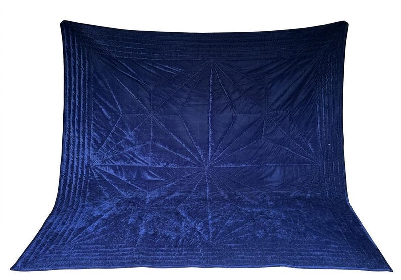 May include: A deep navy blue velvet quilt featuring a geometric starburst pattern created by intricate stitching. The rectangular textile has a soft, reflective surface with parallel quilted lines along the borders and a central radiating design.