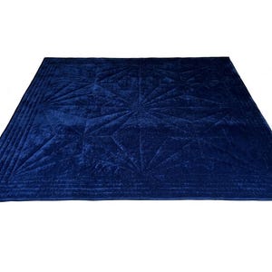 May include: A square, deep blue velvet quilt featuring a geometric starburst pattern stitched across the surface. The edges are finished with multiple parallel rows of straight-line quilting, creating a textured border around the central design.