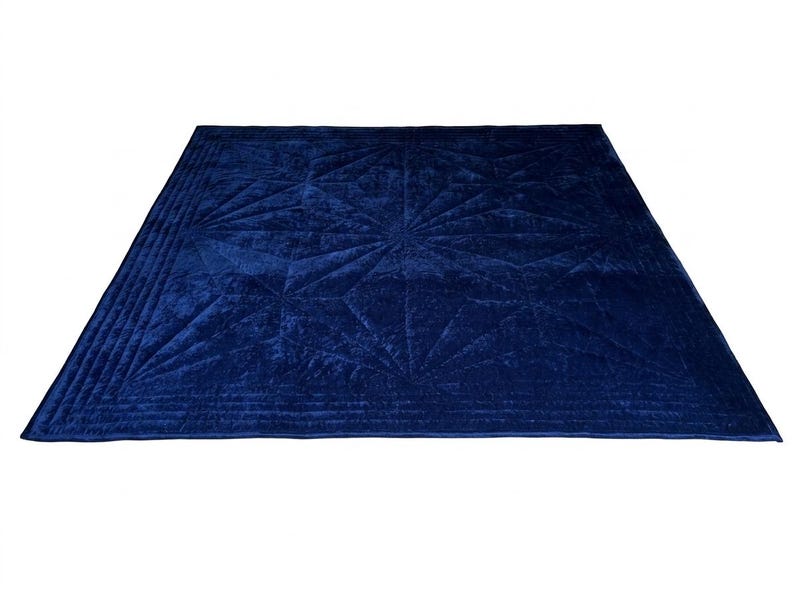 May include: A square, deep blue velvet quilt featuring a geometric starburst pattern stitched across the surface. The edges are finished with multiple parallel rows of straight-line quilting, creating a textured border around the central design.