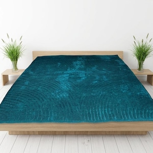 May include: A deep teal velvet quilt featuring a textured, stitched pattern of concentric semicircles. The quilt is draped over a low-profile wooden bed frame, creating a rich, saturated focal point with its dark blue-green color and soft sheen.